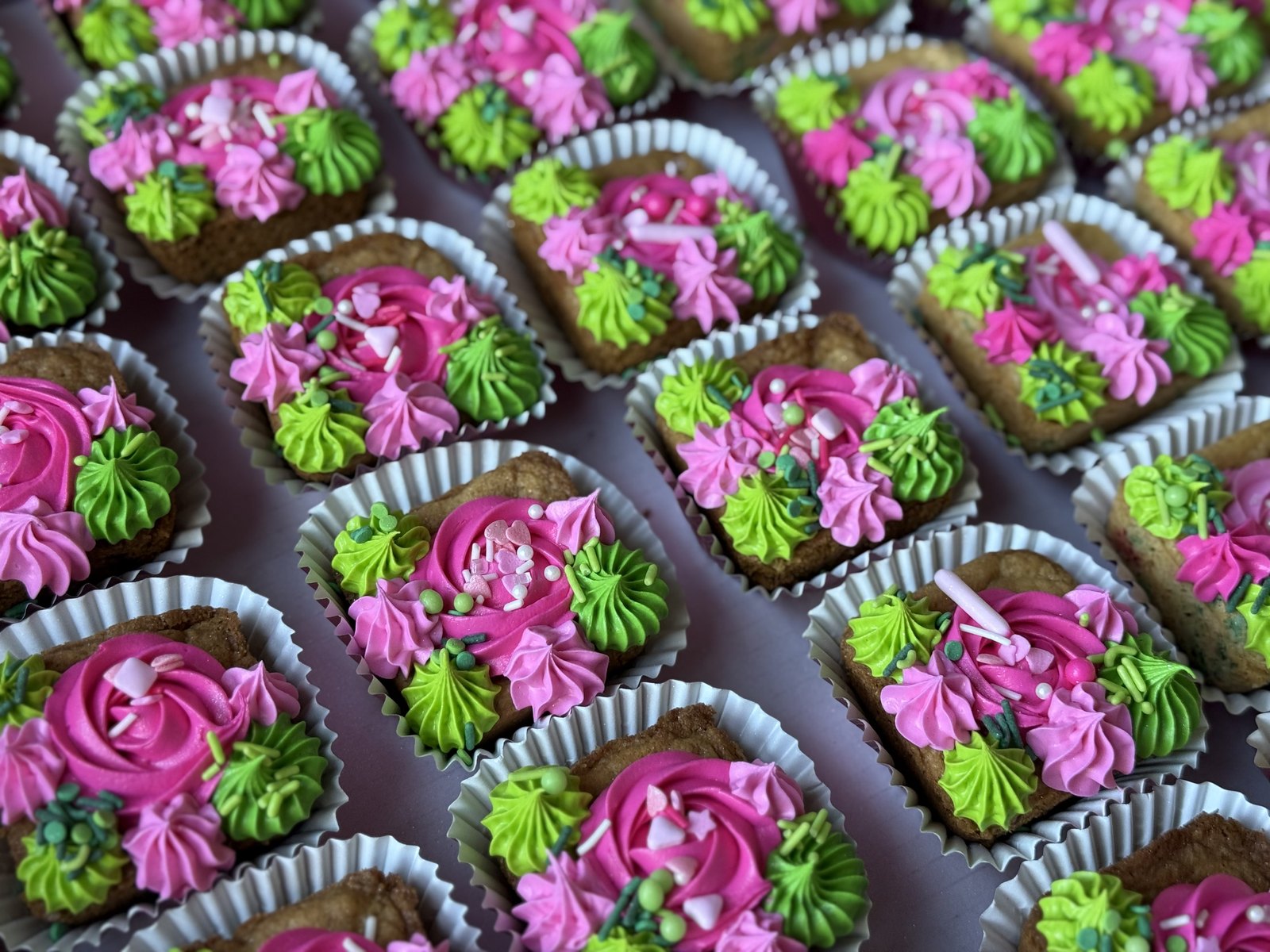 Rows of small cookie bites decorated with pink and green buttercream