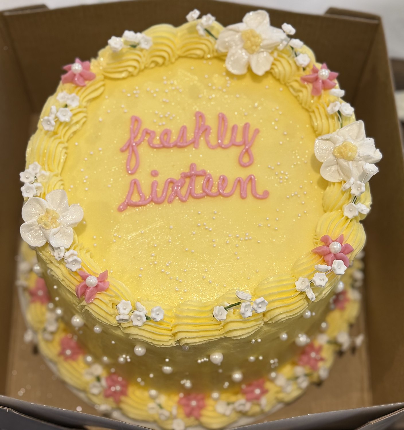 Yellow buttercream birthday cake with white flowers and pearl details